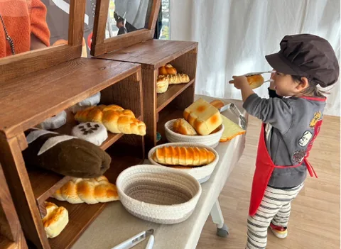 パン屋さんの棚におもちゃのパンを並べる子ども